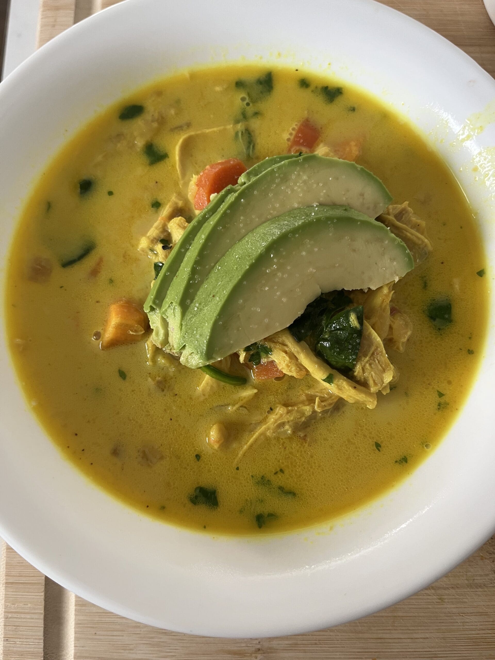 Nourishing coconut chicken soup made with bone broth, turmeric, sweet potatoes, spinach, and shredded chicken topped with sliced avocado.
